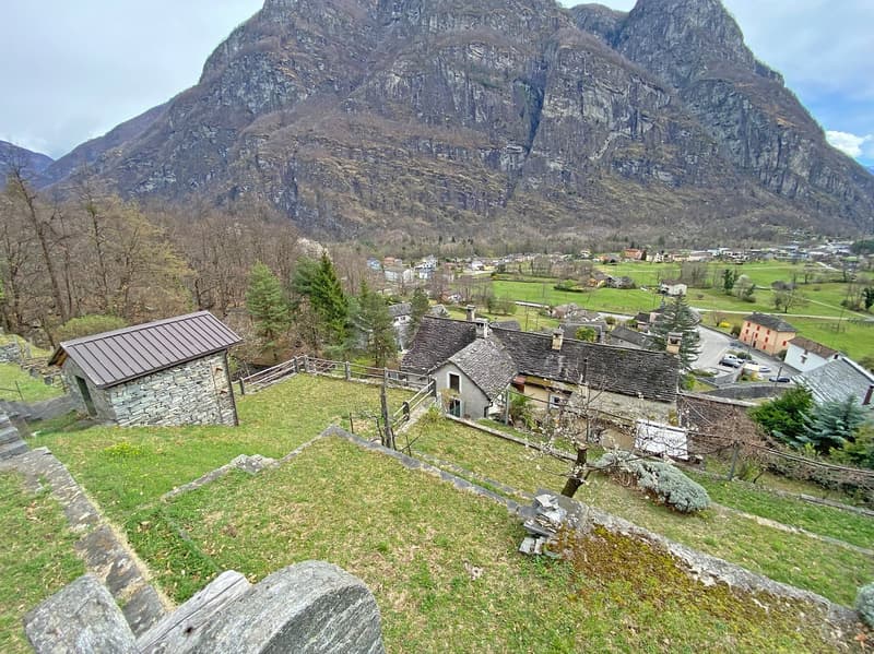 Stone house with a brown roof, surrounded by a fence, with a mountain in the background