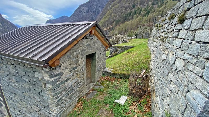 Stone house, metal roof, wooden door, surrounded by grass and mountains