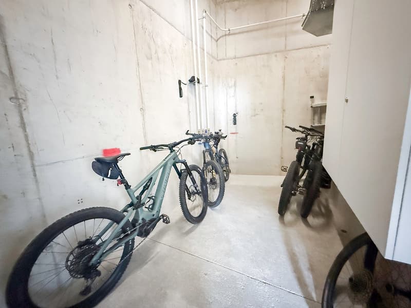 A room with white walls and concrete floor, three bicycles are parked in the room