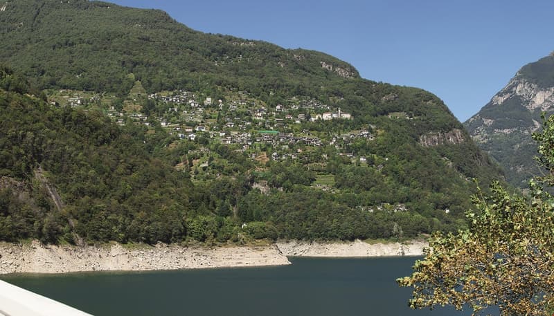 Townhouses, villas, and houses are built on the slopes of a mountain, near a lake.