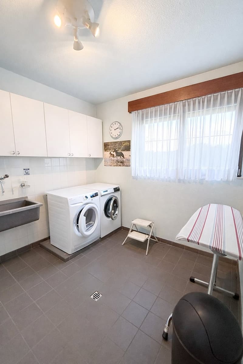 white cabinets, white washing machine, white dryer, sink, ironing board, trash can, clock, window with curtains