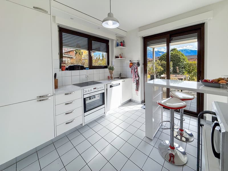 modern kitchen with white cabinets, white tiled floor, white appliances, large windows, sliding glass doors, bar stools, bowl of fruit on counter
