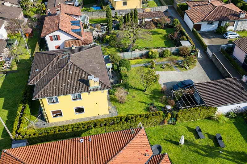 Aerial view of a neighborhood with several houses, each with a different color and style, surrounded by well-maintained lawns and gardens, with a car parked in the driveway of one of the houses.