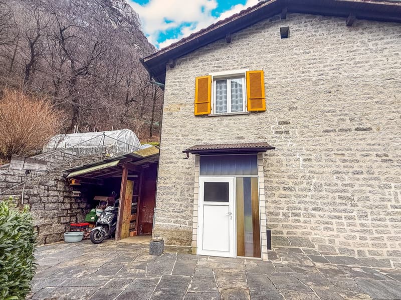 Stone house, yellow shutters, white door, garage with motorcycle, garden with plants