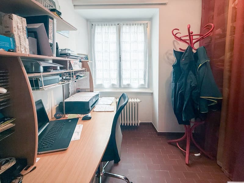 small office room with desk, chair, laptop, shelves, window, and coat rack