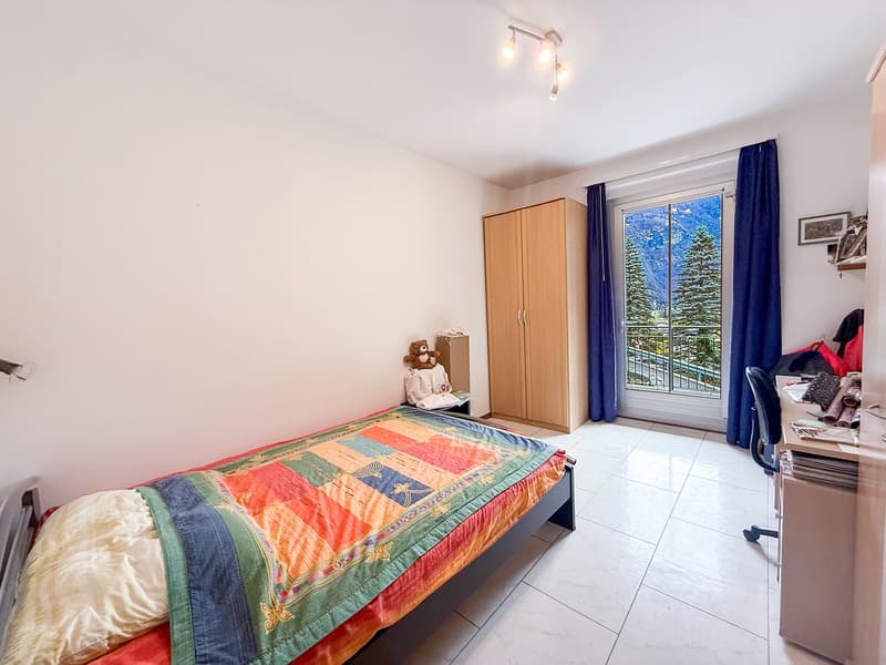 Single bed, wooden cabinet, desk with chair, small table, wall mounted light, glass door