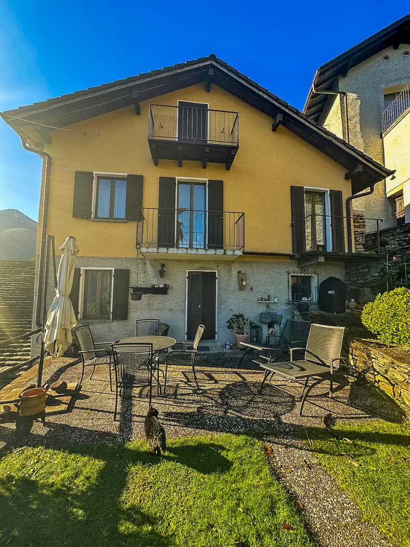 2 story house, yellow exterior, black shutters, balcony, patio with table and chairs, potted plants