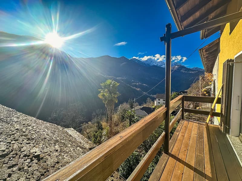 Wooden deck with a cross overlooking a mountainous landscape with palm trees and a bright, sunny sky