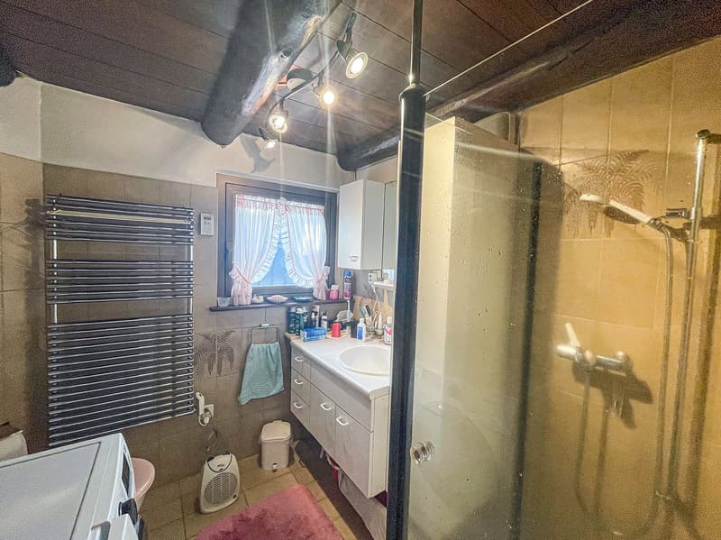 Bathroom with vanity, mirror, and various personal care items. Exposed ceiling beams and pipes. Washer/dryer unit visible.