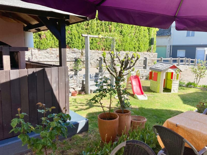 Covered patio area, potted plants, children's playhouse, grassy lawn, stone wall