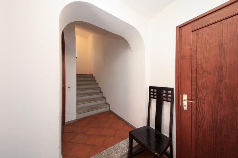 raised ground floor, wooden chair, door, white walls, brown tiled floor, staircase