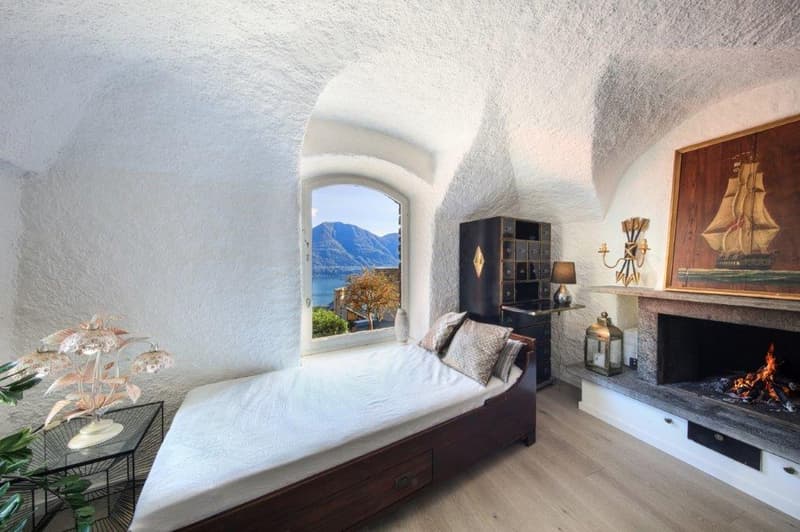 small single bed, fireplace, large window with a view, wooden floor, plant, white walls
