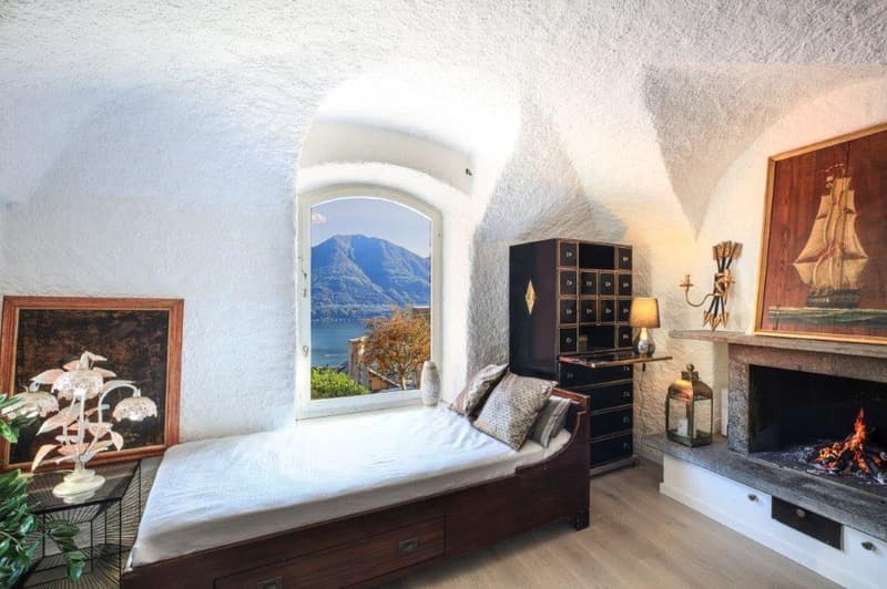 a cozy room with fireplace, bed, side table with lamp, plant, picture frame, and cabinet with drawers