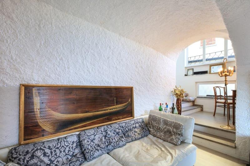 White couch, large art piece on wall, staircase, table, chandelier