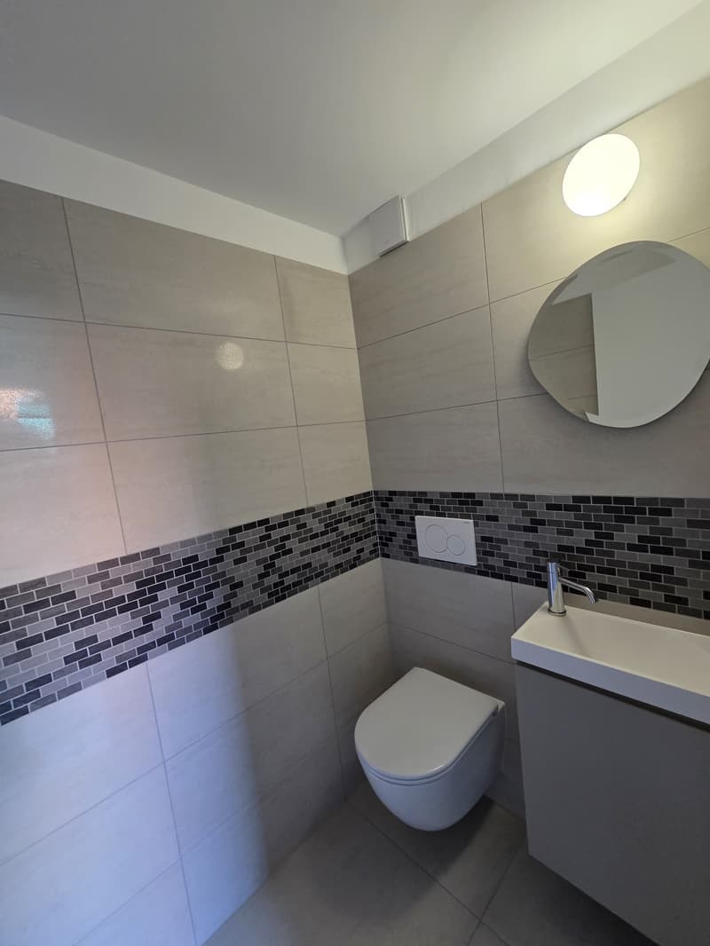 Bathroom with white tiles, white toilet, white sink, round mirror, wall-mounted light