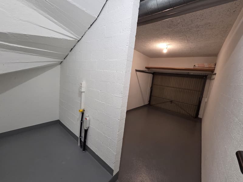 Empty room with white walls, gray floor, a garage door, and a ceiling light