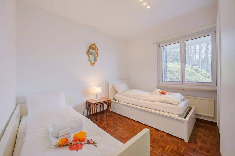 Two twin beds, nightstand, small table, mirror, window, radiator, wooden floor