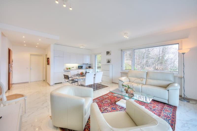 white leather couches, round glass table, white armchairs, rug, kitchen, dining area, trees