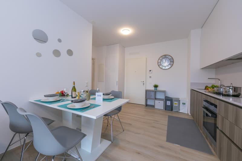 Wooden floor, white walls, gray chairs, white table, white kitchen cabinets, clock on wall