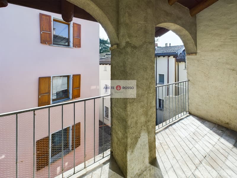 Two-story building with arched entryways, white walls, wooden shutters, and a balcony or terrace on the upper level.