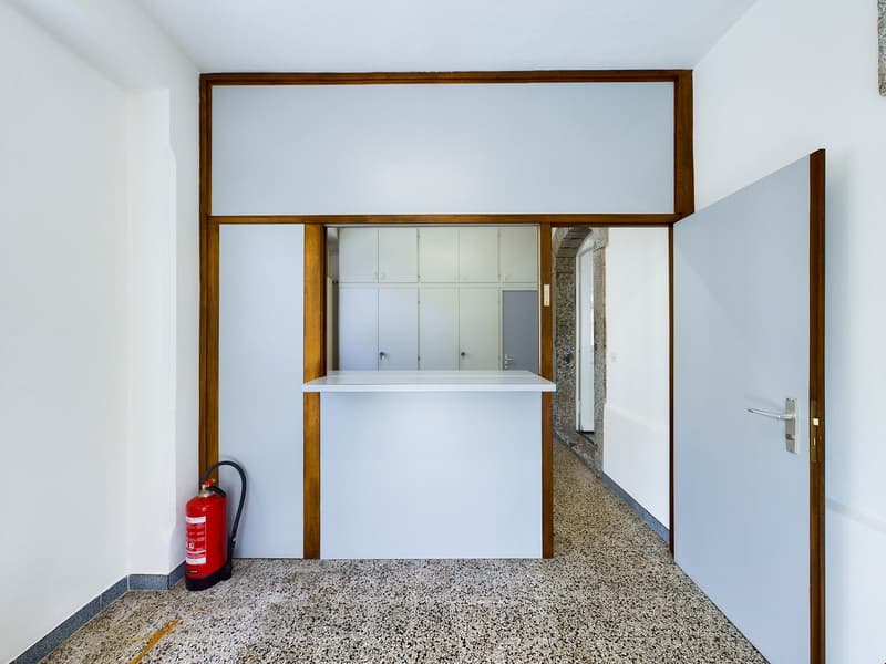 The image shows a hallway or entryway with a wooden frame and shelving unit. The floor is made of terrazzo or a similar speckled material. A fire extinguisher is visible in the corner.