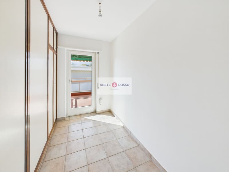 The image shows a hallway with a tiled floor, white walls, and a sliding door. There is a sign for 'Abete Rosso' on the wall.