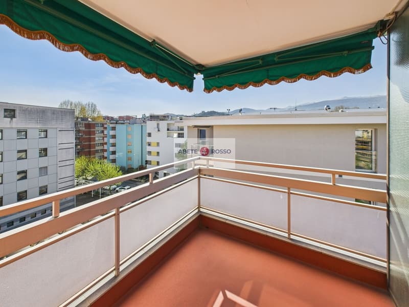 Spacious balcony with green and orange awning, overlooking a residential area with multi-story buildings