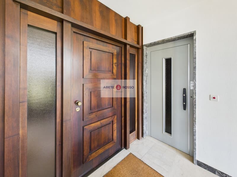 Wooden paneled entrance with a glass door, marble flooring, and a security system panel visible.