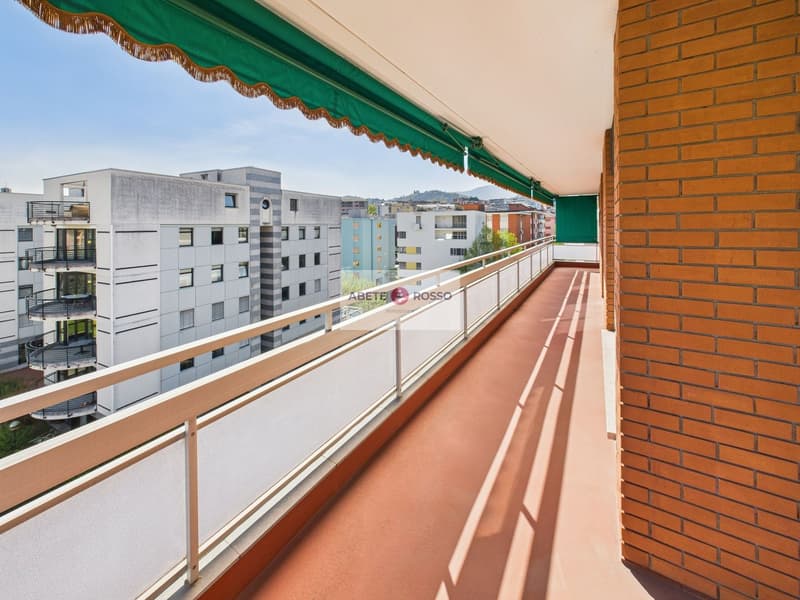 Spacious balcony with a green awning, overlooking a residential area with modern apartment buildings