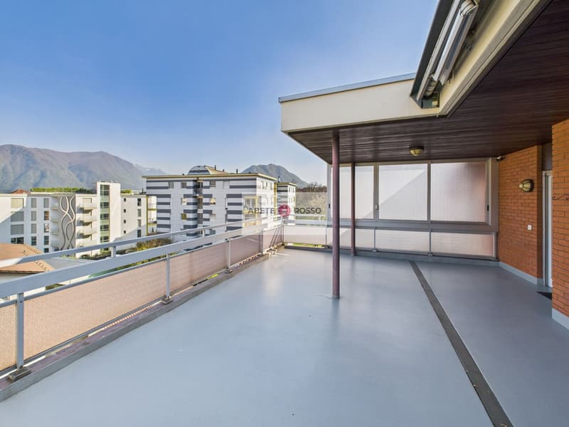 Spacious balcony with concrete flooring, metal railings, and a view of the surrounding buildings and mountains in the distance.