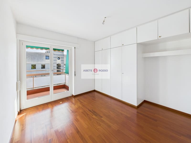 Spacious bedroom with hardwood flooring, white walls, built-in wardrobes, and a balcony with a view.