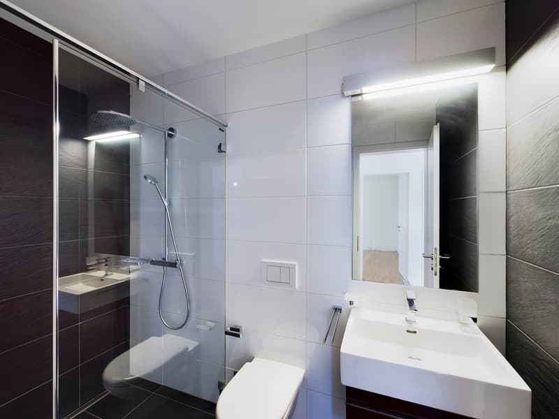 modern bathroom with glass shower, white sink, mirror, and tiled walls