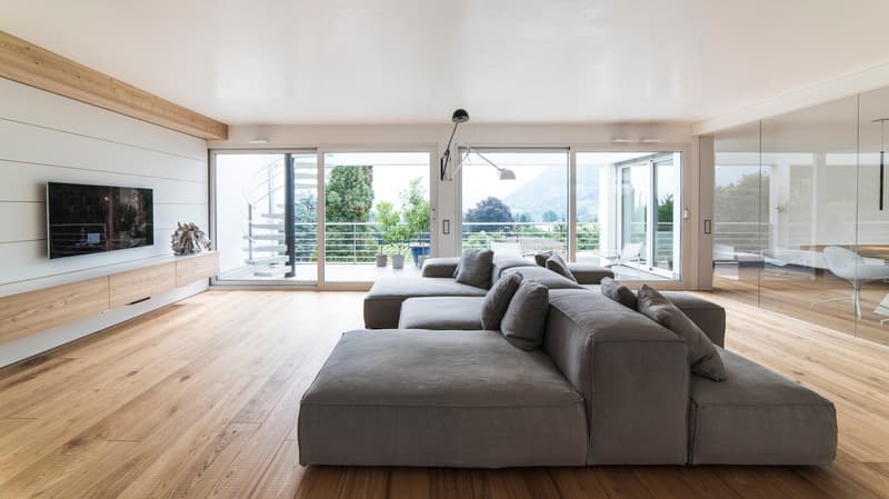 Wooden floor, large grey couch, TV, sliding glass doors to balcony