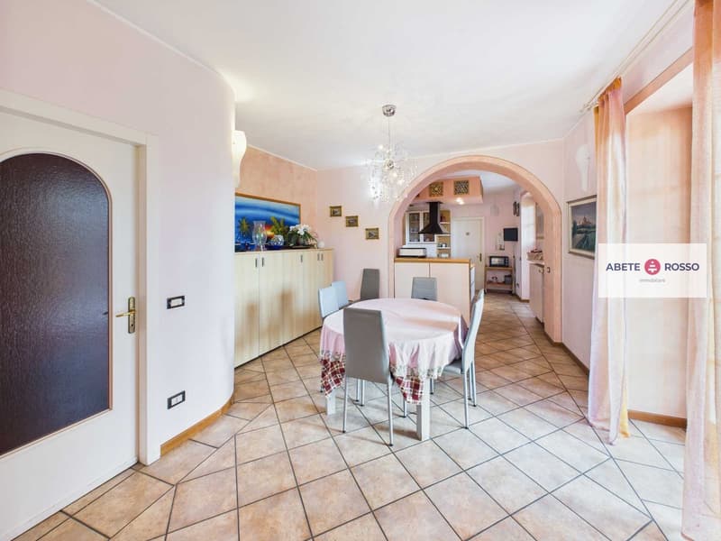 Dining room with tiled flooring, table, chairs, arch, cabinets, decorative items, microwave, refrigerator.