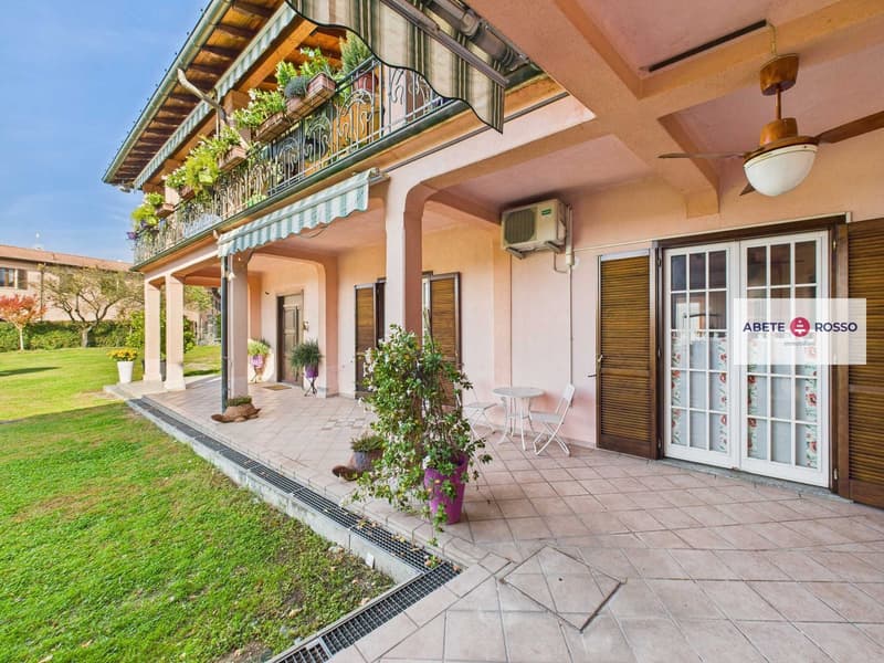 Terraced house with pink exterior, white doors, awning, plants on the balcony, outdoor seating area, garden in front.