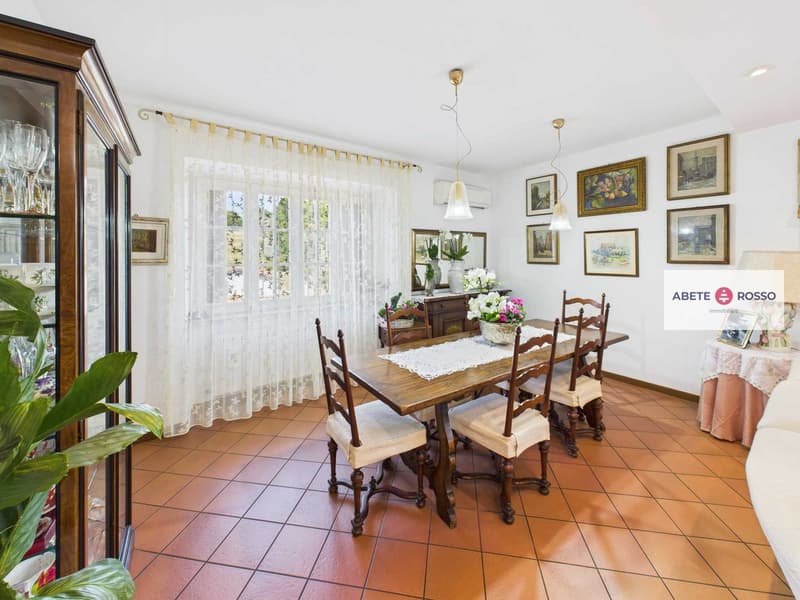 Dining room with a wooden table, cushioned chairs, decorative plant, wine glasses, and artwork on the wall.