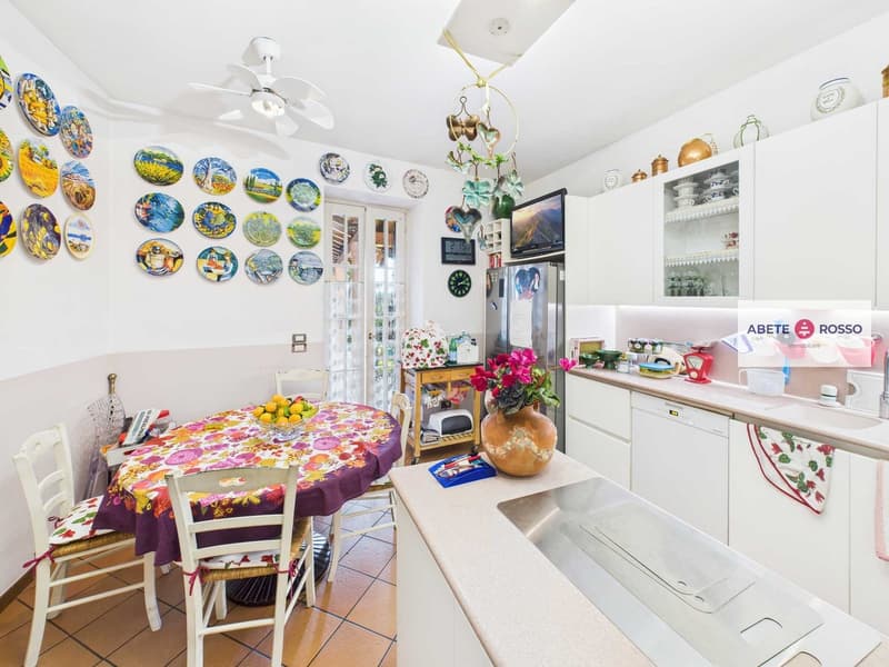 Modern kitchen with white cupboards, modern appliances, a dining table and chairs, and ceramic wall plates
