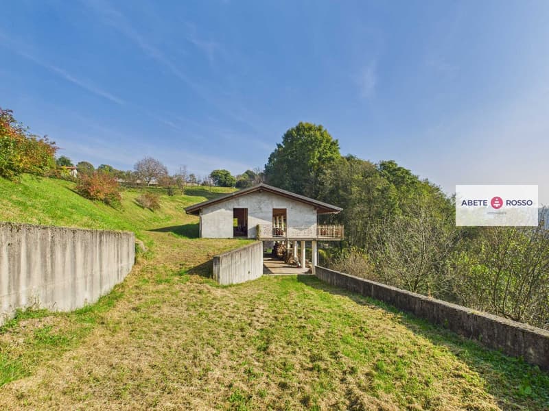 A house situated on a slope with a balcony, concrete retaining walls, greenery around