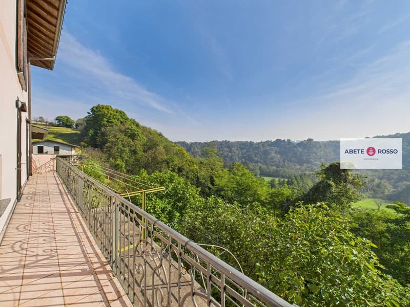 elevated view of a house with a balcony, railing, and surrounding trees and hills