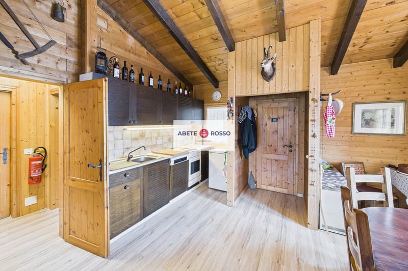 kitchen with wooden walls, wooden floor, sink, oven, refrigerator, wine bottles, fire extinguisher, wooden dining table and chairs