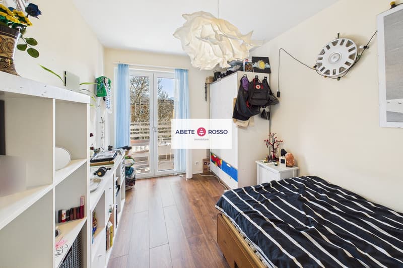 bedroom with bed, wooden floor, sliding glass door to balcony, white shelves, decorative items