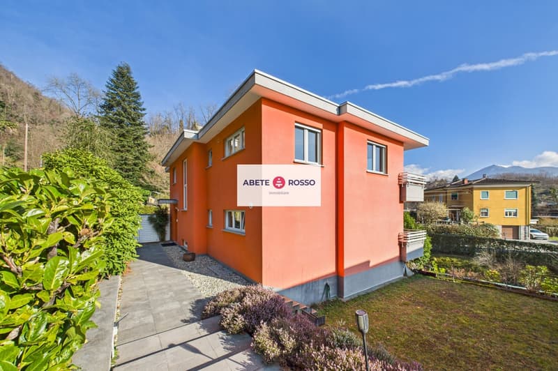 Two-story house, orange exterior, white trim, multiple windows, balcony, gravel driveway, garden, greenery