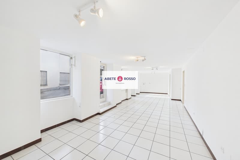 Empty hallway with white tiles, white walls, ceiling lights, windows with blinds