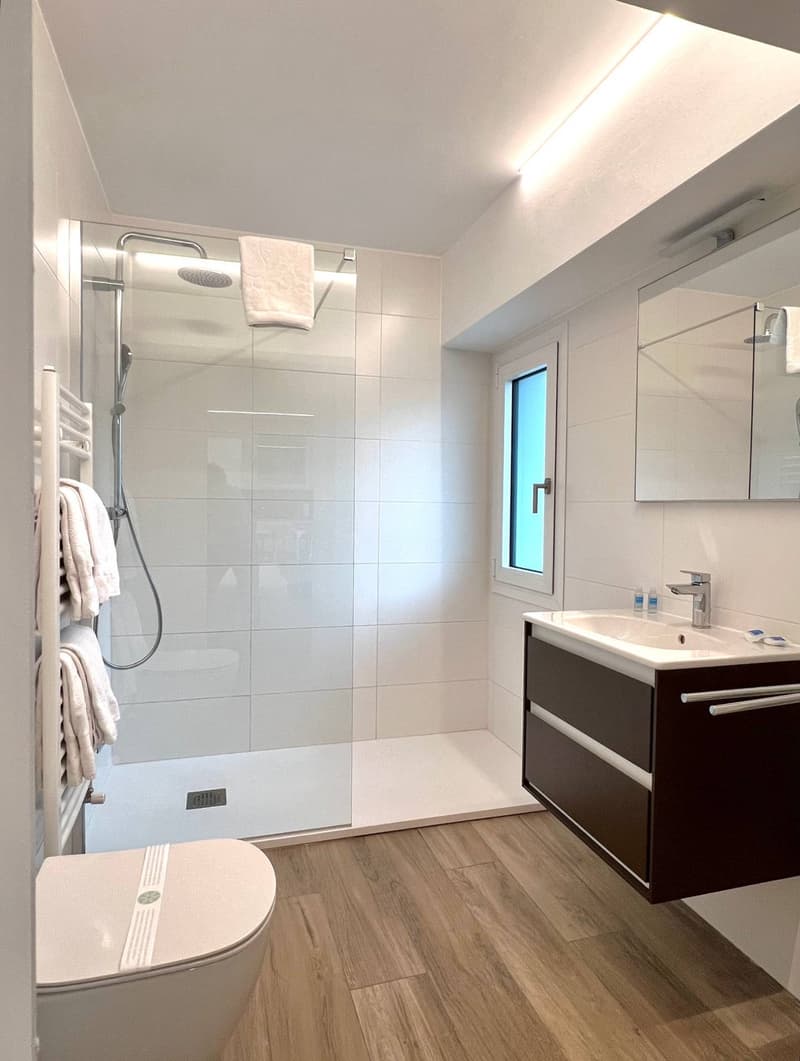 Modern bathroom with white tiled walls, wood-look flooring, vanity with sink, and a glass-enclosed shower area