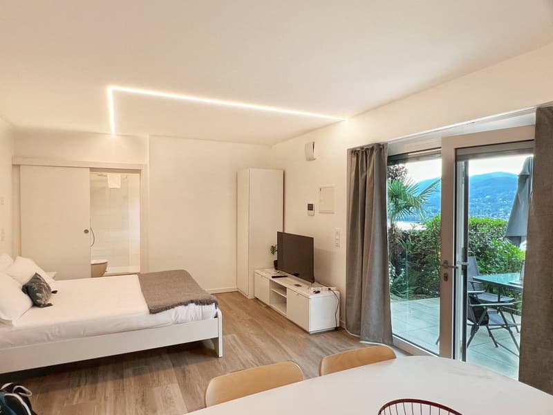 Spacious bedroom with large windows overlooking a scenic outdoor view, hardwood flooring, a TV stand, and a balcony or terrace area.