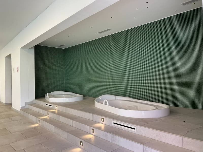 Two white Jacuzzi bathtubs against a green mosaic wall, raised flooring, ambient lighting