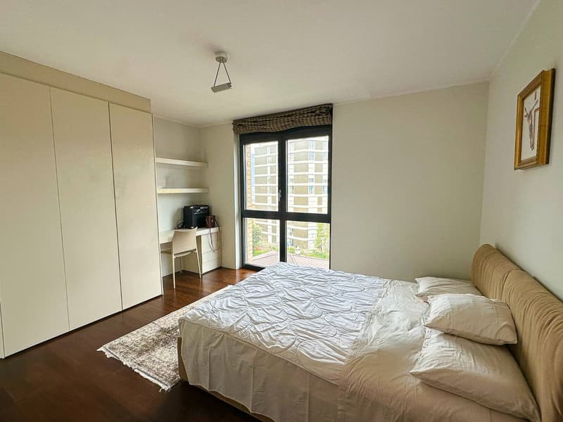 Spacious bedroom with large windows, built-in wardrobe, desk, and hardwood flooring.