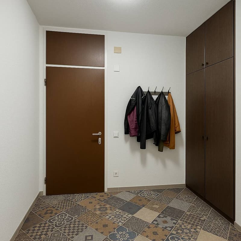 Large brown wooden door, brown wooden cabinets, white walls, decorative tiled floor, jacket rack on the wall with a few jackets