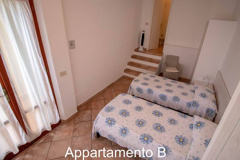 Bedroom with two beds, white walls, wooden floor, bathroom, staircase