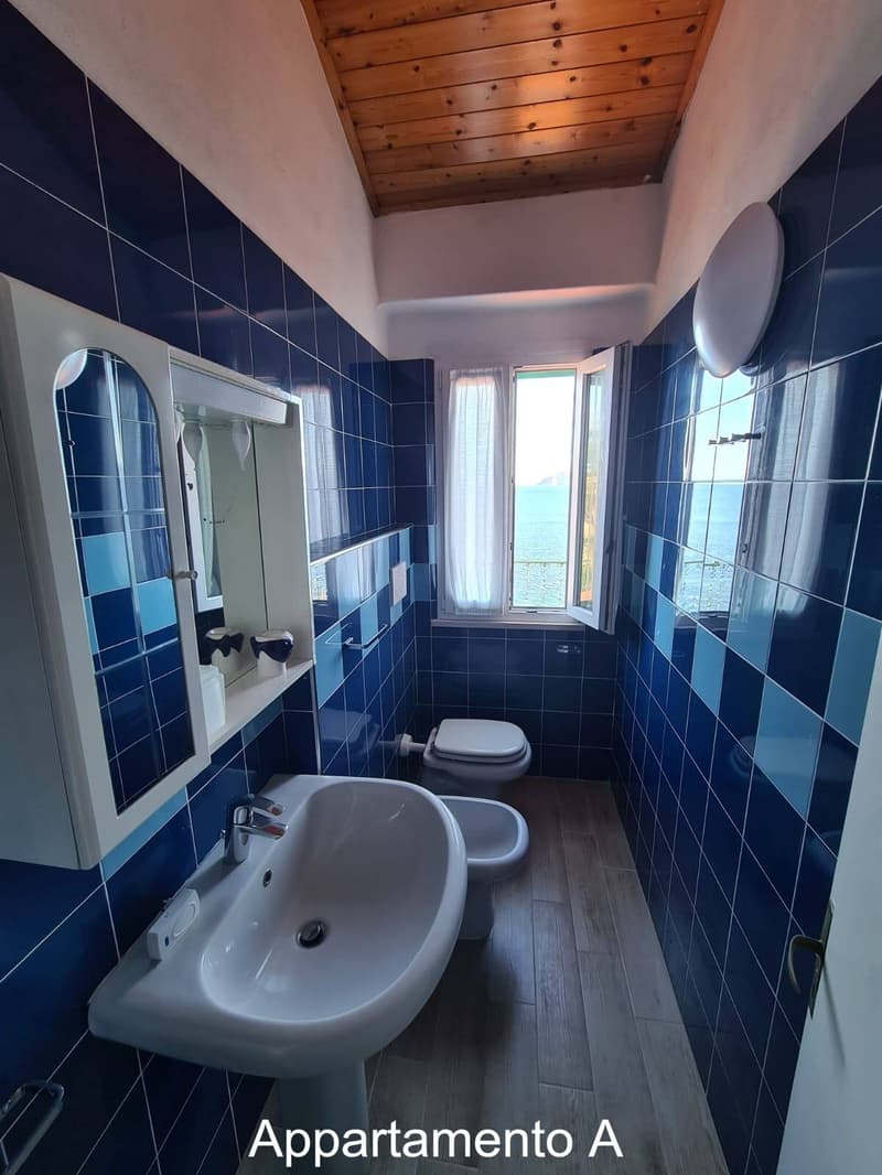 A small bathroom with blue tiles, a sink, a toilet, a window, and a mirror.